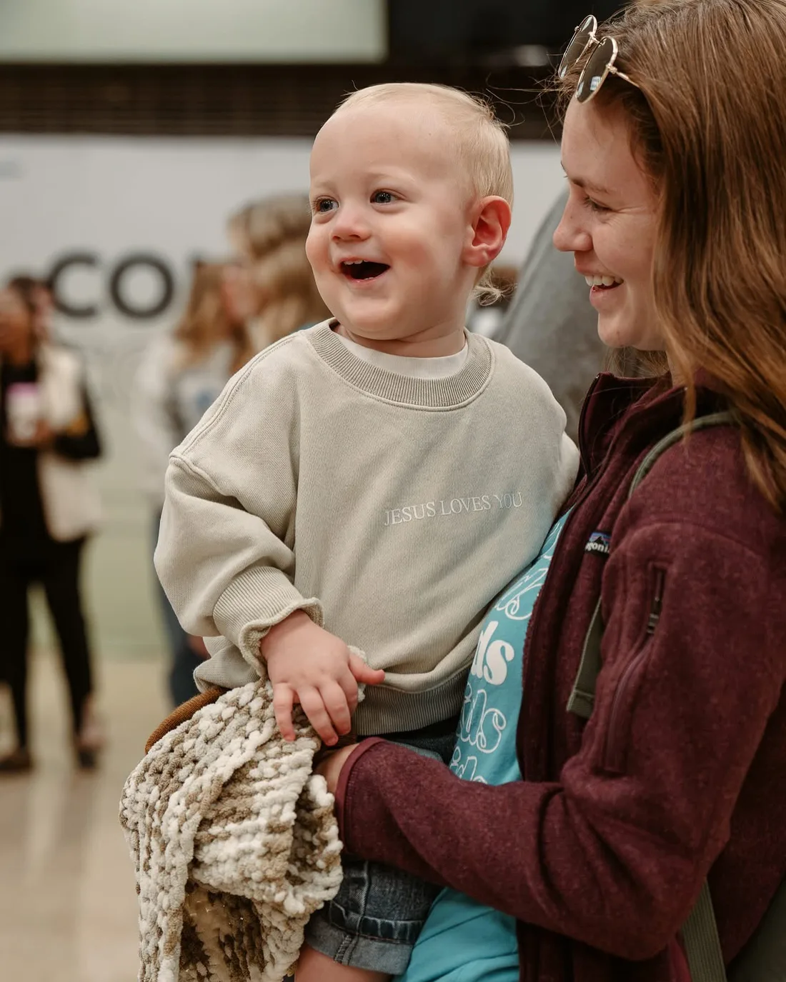 Laughing toddler in a Jesus Loves You sweatshirt with a Nuvo Kids volunteer in Dublin, Ohio