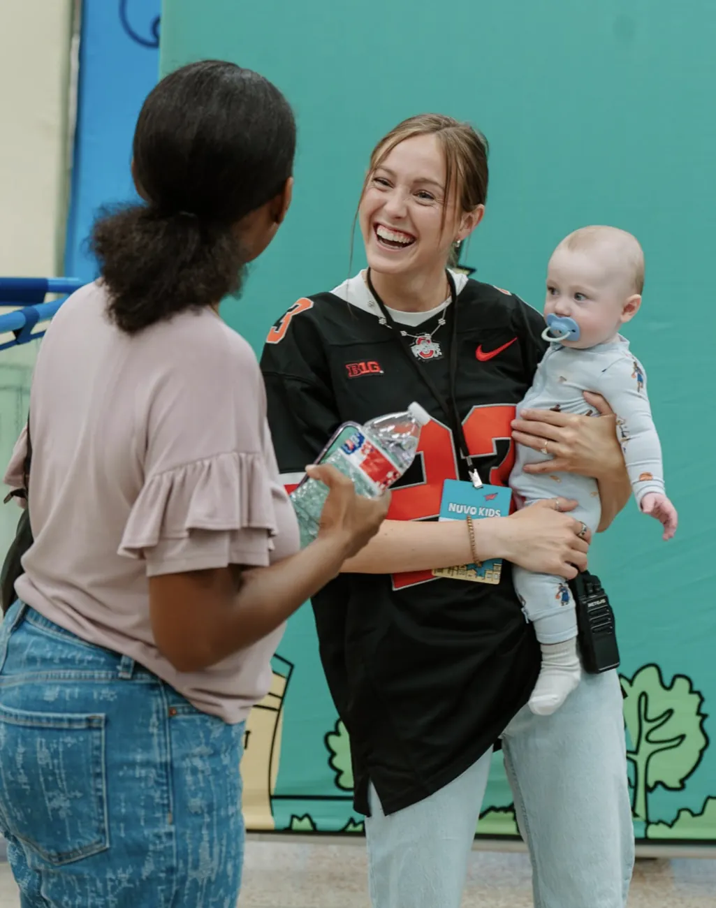 Smiling Nuvo Kids volunteer holding a baby and welcoming a parent at church in Dublin, Ohio