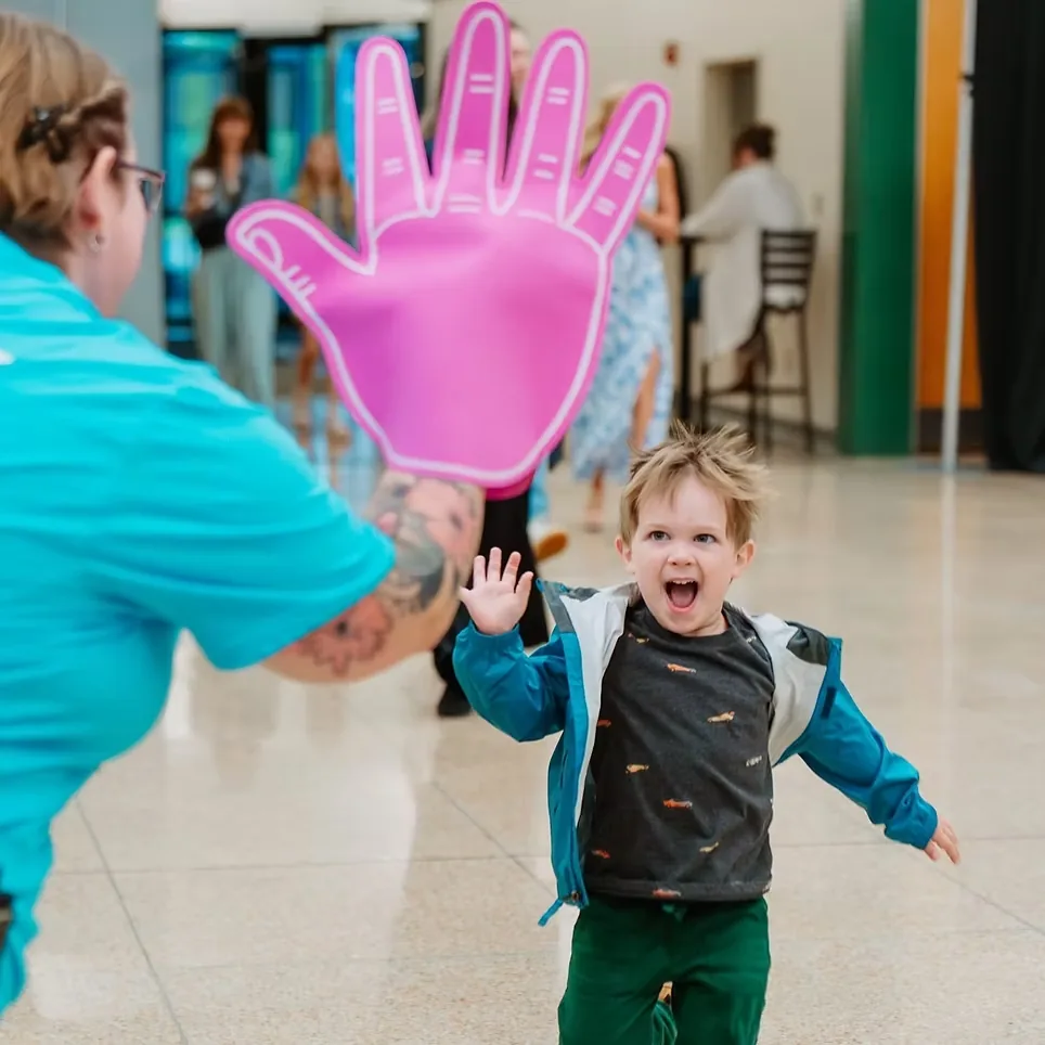 Toddler running to high-five a Nuvo Kids volunteer's foam hand at check-in in Dublin, Ohio